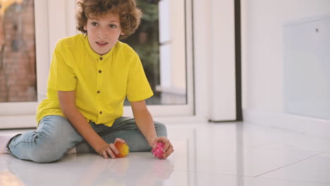 blond boy with curly hair kneeling on the floor while playing with balls with his dog 1