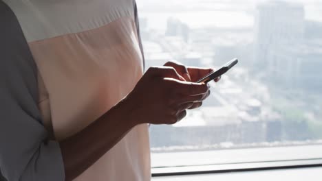 midsection of african american businesswoman using smartphone at window