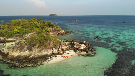 Aerial-footage-of-a-small-island-approaching-a-white-shirtless-man-on-top-of-rocks