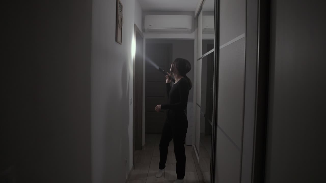 retrato de una mujer con una linterna buscando algo dentro del callejón oscuro de la casa