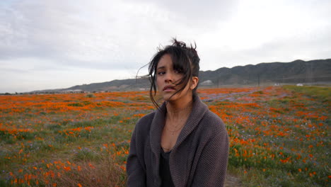 young beautiful woman crying and looking sad in a meadow of wild flowers under dark cloudy skies in slow motion