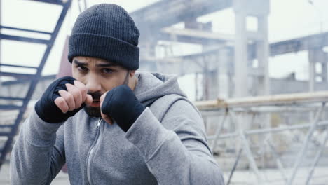 handsome bearded caucasian man boxing to the camera outdoors an abandoned factory on a cloudy morning