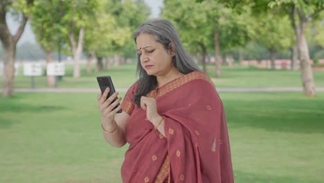 Indian-old-woman-scrolling-through-phone-in-park