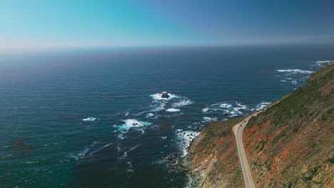 rocky shore with highway over cliffs. beautiful endless blue pacific ocean interflowing with clear azure sky. aerial view.
