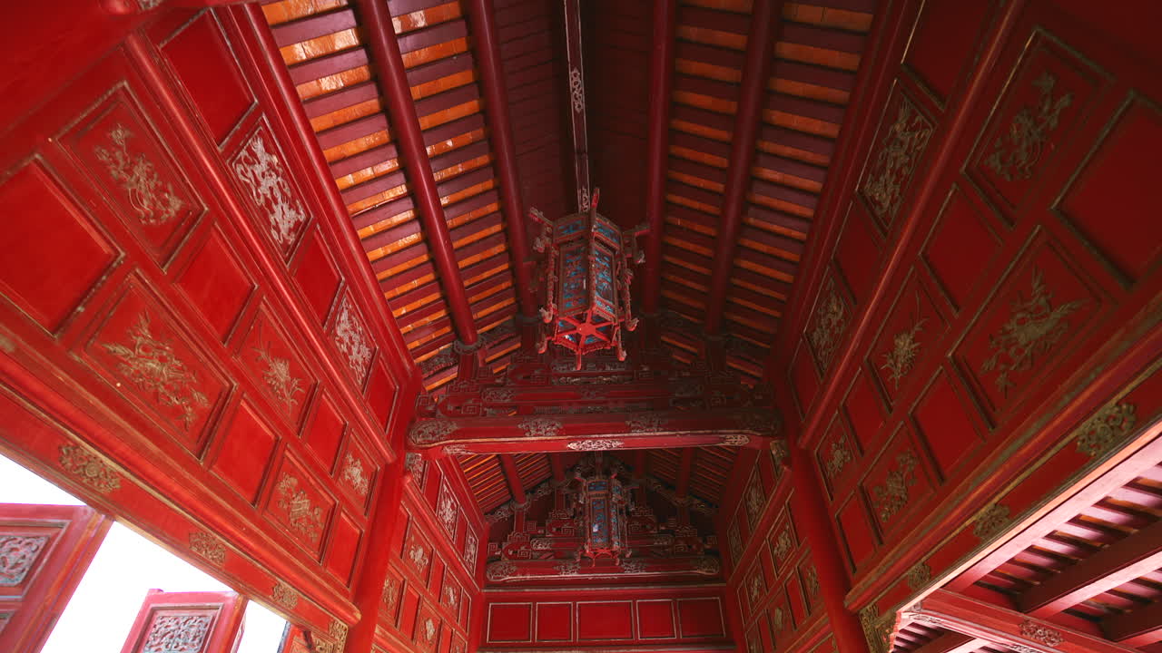 Et interiør lavvinkelbillede af det udsmykkede røde og guldlakerede træloft i en paladsbygning i Hue Imperial City, med en traditionel dekorativ lanterne
