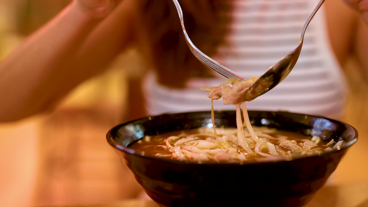 Close-up of a person savoring noodle soup with chopsticks and spoon in a warmly lit Gold Coast setting