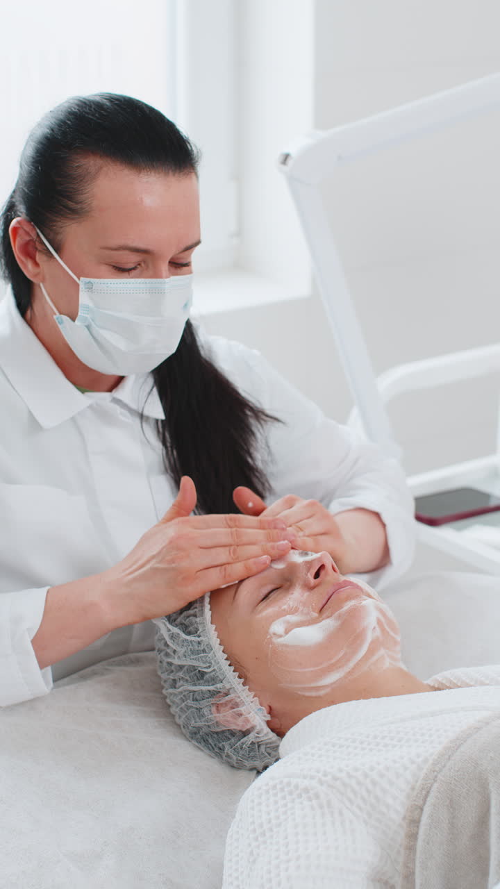 Cosmetologist applying special moisturizing cream scrub peeling face of pretty caucasian woman girl