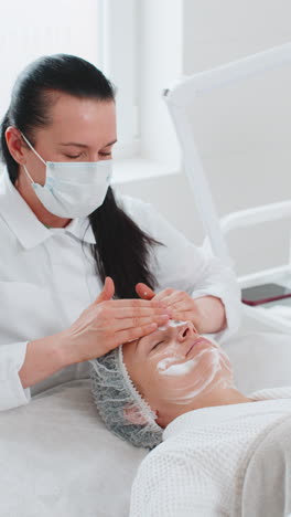 cosmetólogo aplicando crema hidratante especial exfoliando la cara de una bonita mujer caucásica niña