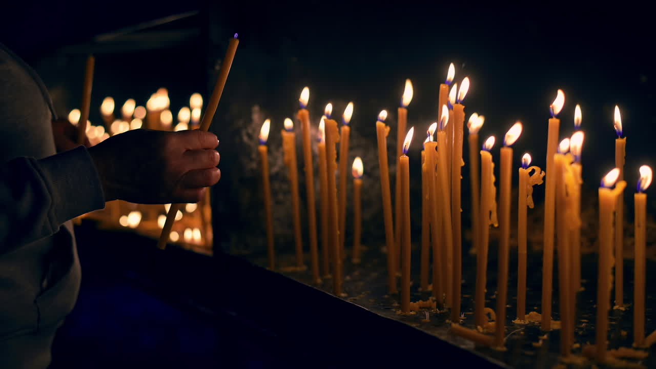 Una persona appicca il fuoco e mette una candela vicino a molte altre candele accese con sfondo nero