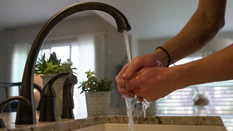 Young-man-washes-dirty-hands-in-kitchen-sink-with-granite-counter-top