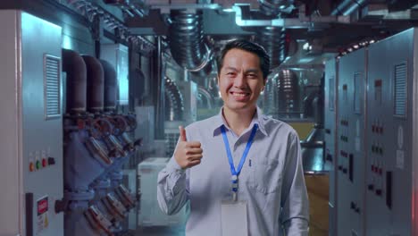 shot captures of an asian male professional worker standing in engine control room, his broad smile at the camera and thumbs up