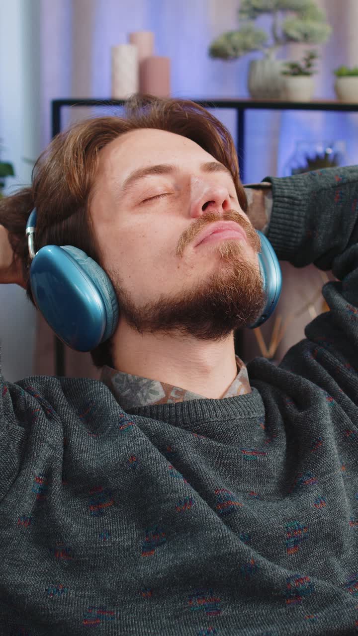 hombre caucásico feliz con auriculares inalámbricos bailando escuchando música rock n roll favorita en el sofá de casa