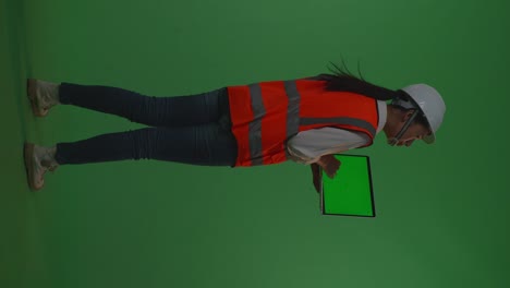 back view of full body asian female engineer with safety helmet working on a green screen laptop and looking around while standing in the green screen background studio, during sunset or sunrise time