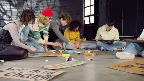 jóvenes activistas ambientales pintando carteles sentados en el suelo