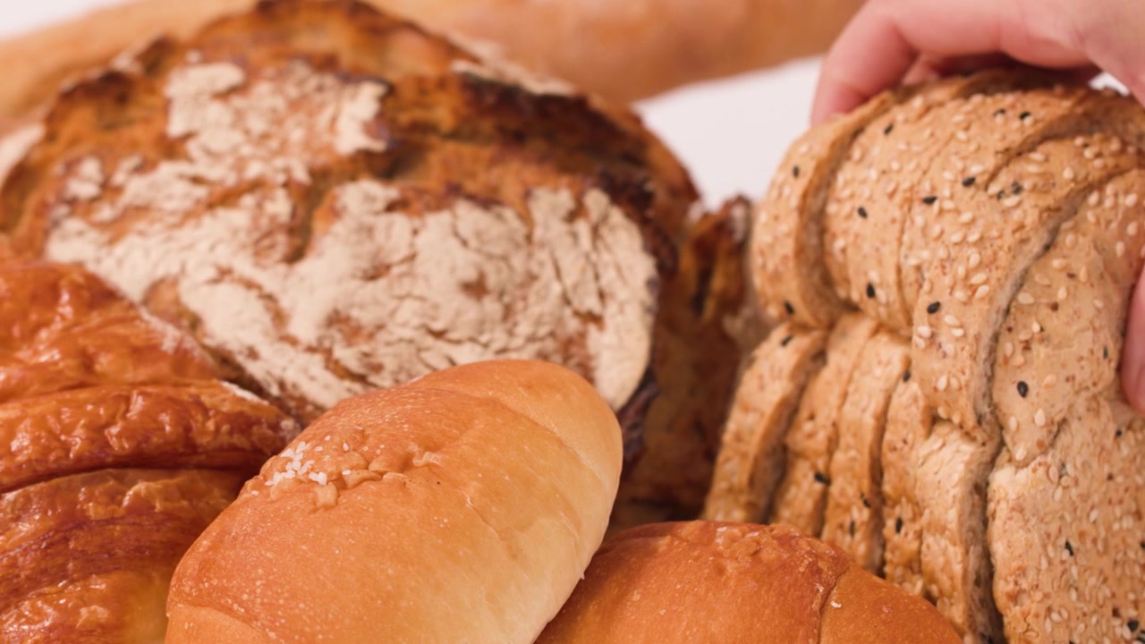 Close-up shot of hand selecting sliced multigrain bread from diverse fresh bakery products.