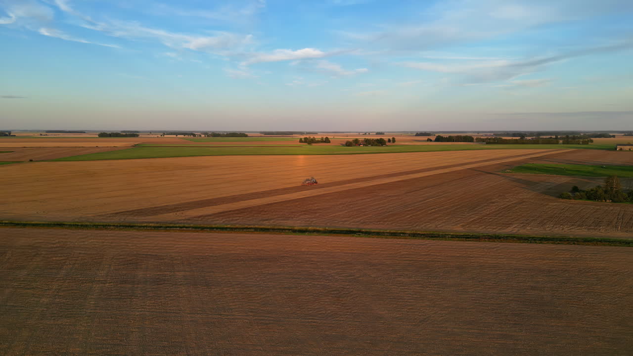 Drohnenaufnahme einer Agrarlandschaft mit braunen Ackerfeldern und grünen Feldern sowie Bäumen im Hintergrund, bei sanftem Licht.