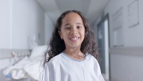 portrait of happy biracial girl looking at camera at hospital, in slow motion