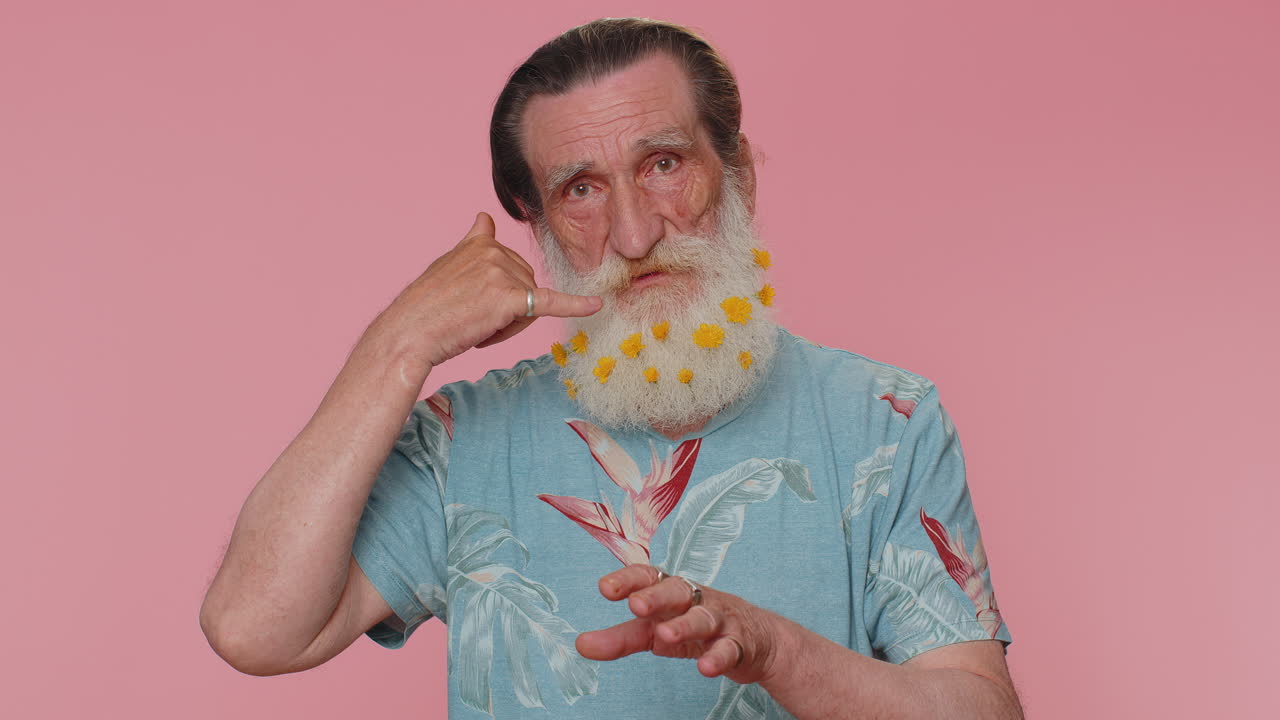 un hombre barbudo de edad avanzada alegre mirando a la cámara haciendo un gesto telefónico como decir hola me llamas