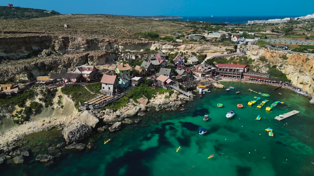 Aerial view of Popeye Village, Malta. Colorful seaside cottages, turquoise waters, and coastal scenery create a charming and playful Mediterranean landscape from above