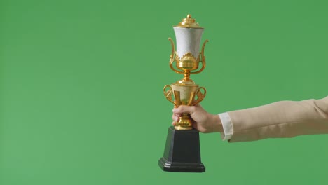 close up of business woman's hand holding a gold trophy to her side showing award winning as the first winner on green screen background in the studio