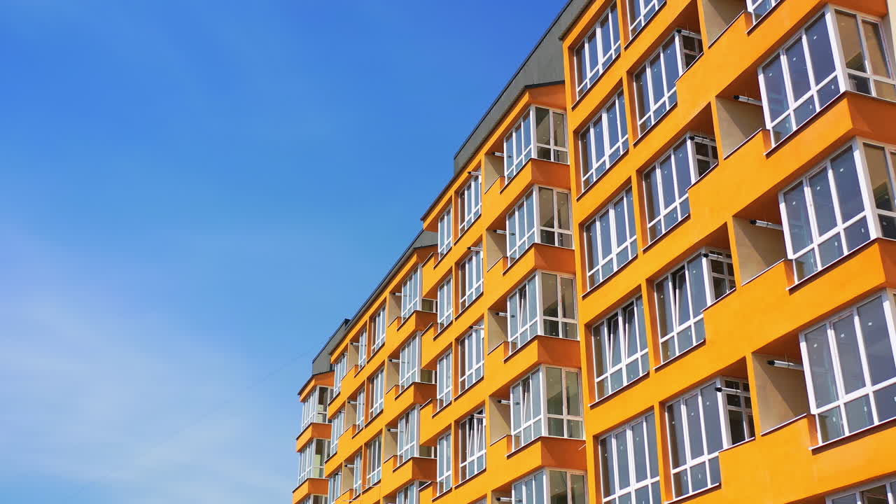 Bright city architecture against blue sky. New apartment building in orange color for urban residents. Modern design of high-rise building.