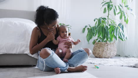 loving mother playing with baby daughter sitting on floor in bedroom