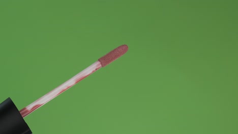 rotación diagonal del pincel de brillo de labios. aislado en verde.