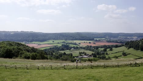 AERIAL---People-walk-their-dog-on-a-hill-near-Uley,-Cotswolds,-England,-tracking-right