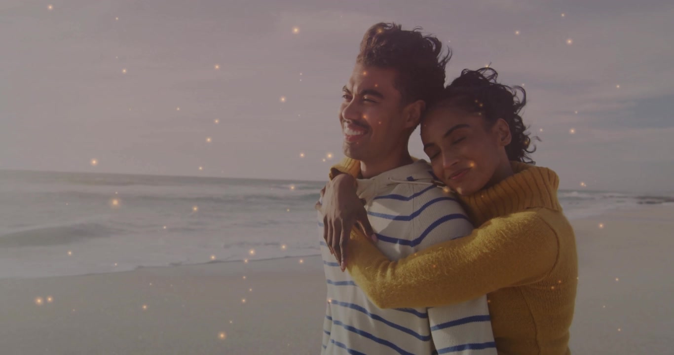 Couple embracing beach shore, animation adding gold particles around them, enhancing romantic mood