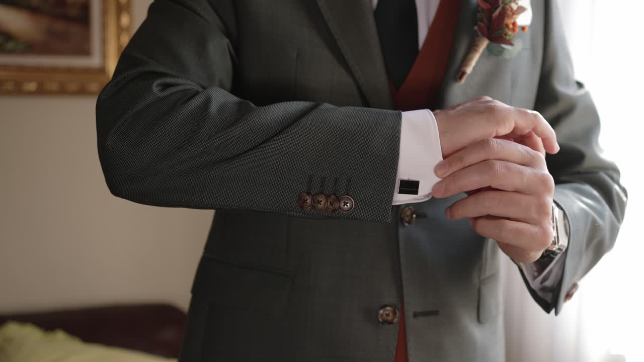Close up of groom adjusting suit sleeve in soft natural light indoors
