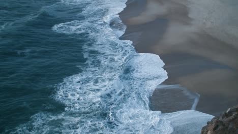 Big-waves-break-on-the-coast-at-Nazare-in-Portugal,-taken-from-above-on-a-late-summer-afternoon