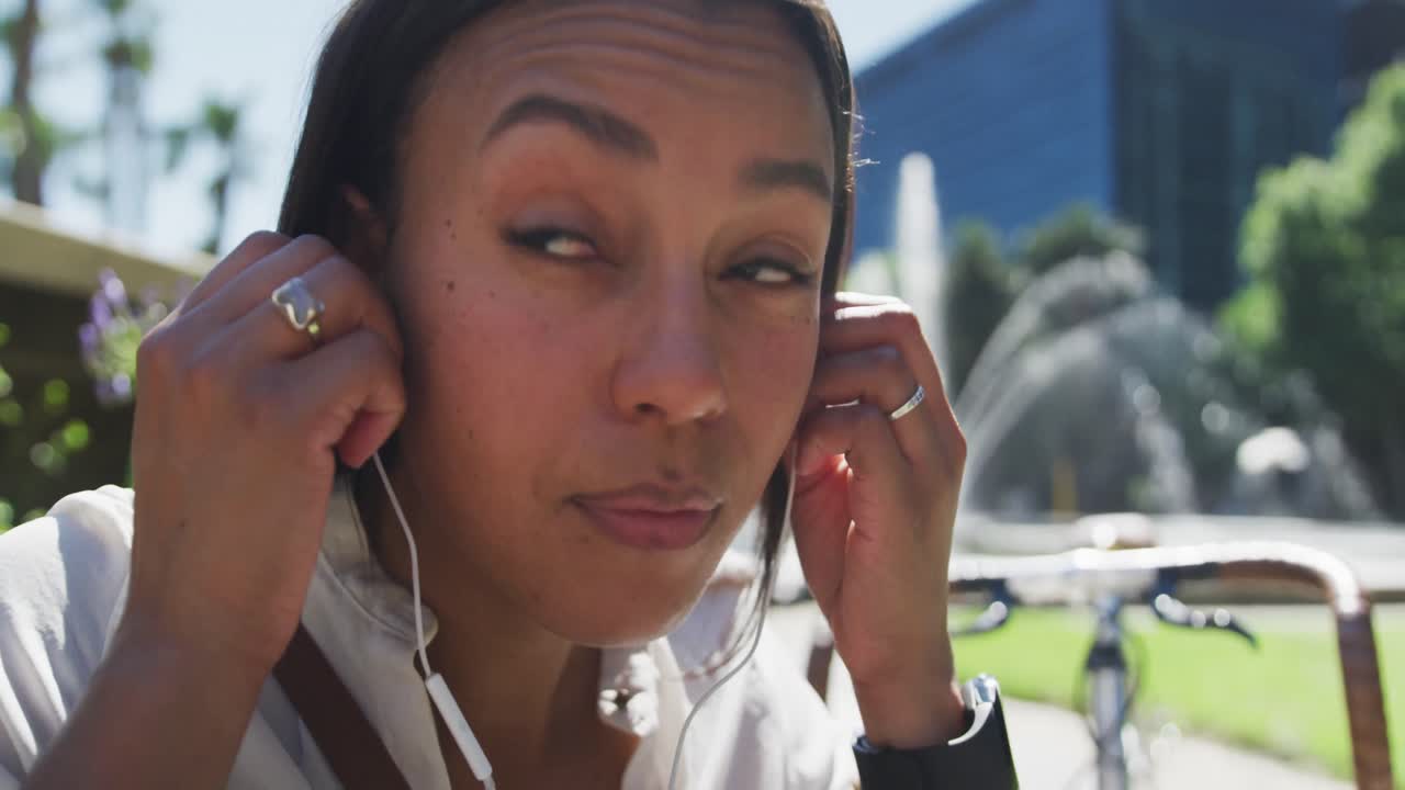 mujer afroamericana poniendo auriculares en el parque de la ciudad