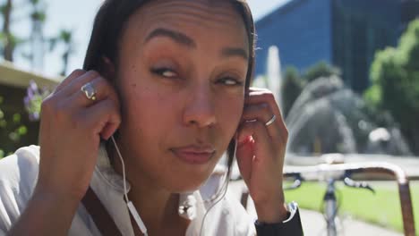 african american woman putting earphones on in city park