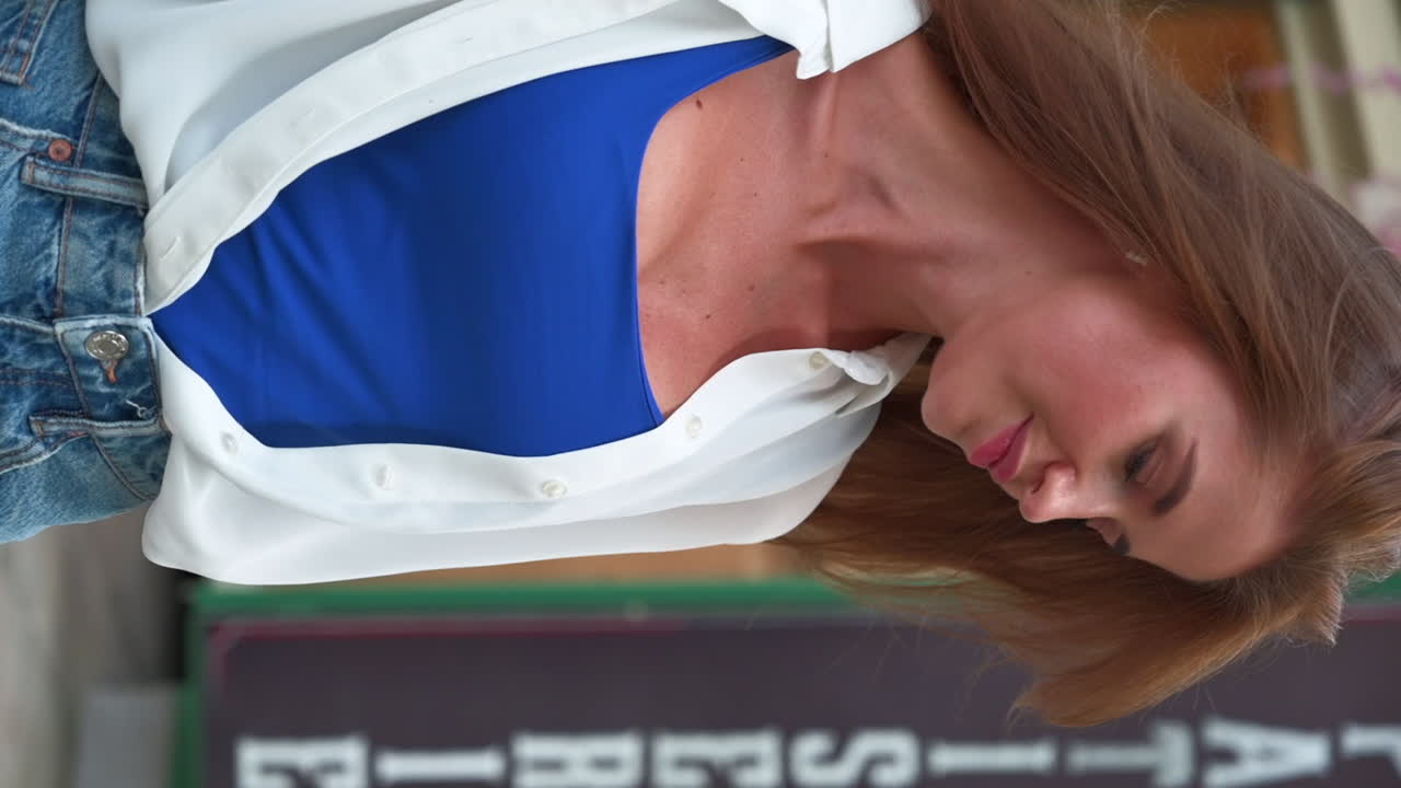 Brunette woman posing and touching up her hair in front of an outdoor cafe. Vertical