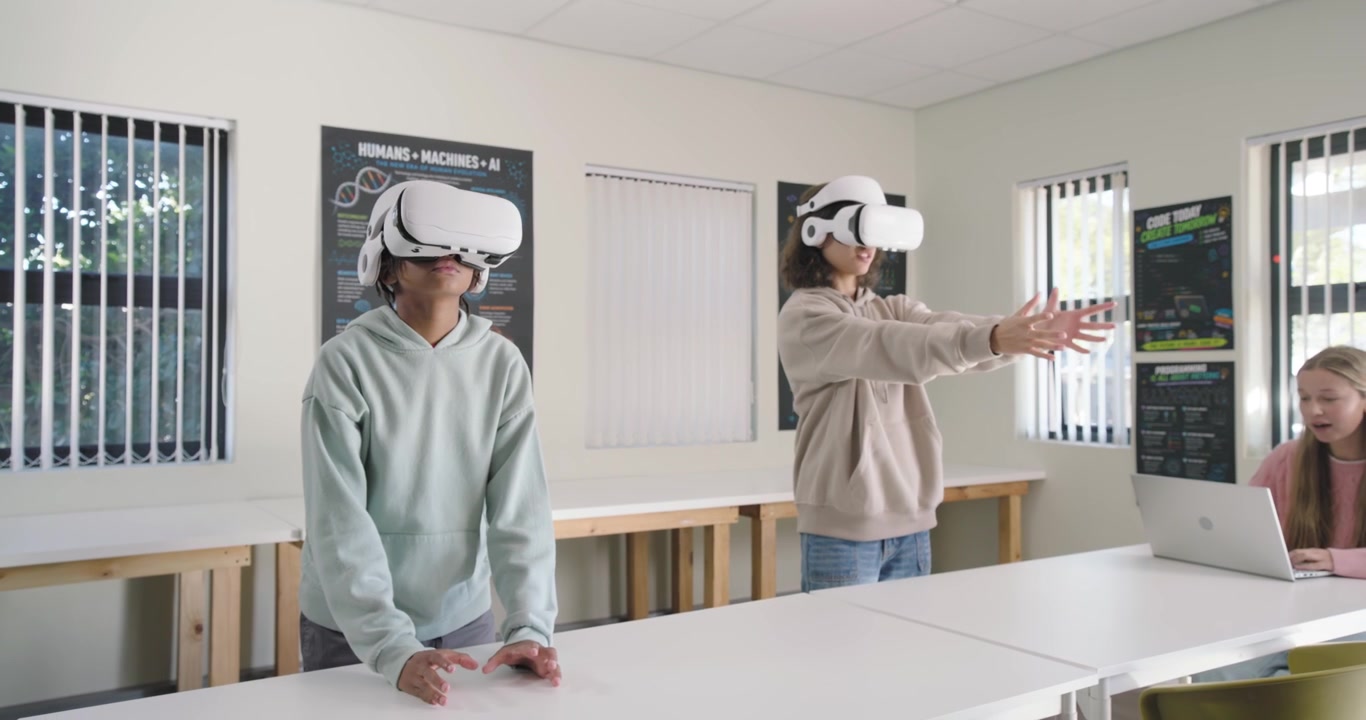 Studenti che indossano visori VR bianchi, con uno spazio VR in laboratorio, mentre un utente di laptop osserva.