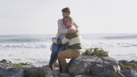 caucasian couple enjoying free time by sea on sunny day sitting and embracing