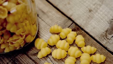 scattered gnocchi pasta on wooden background and tidied on glass jar