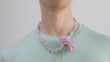 close up young man with necklace and t shirt holding a flower