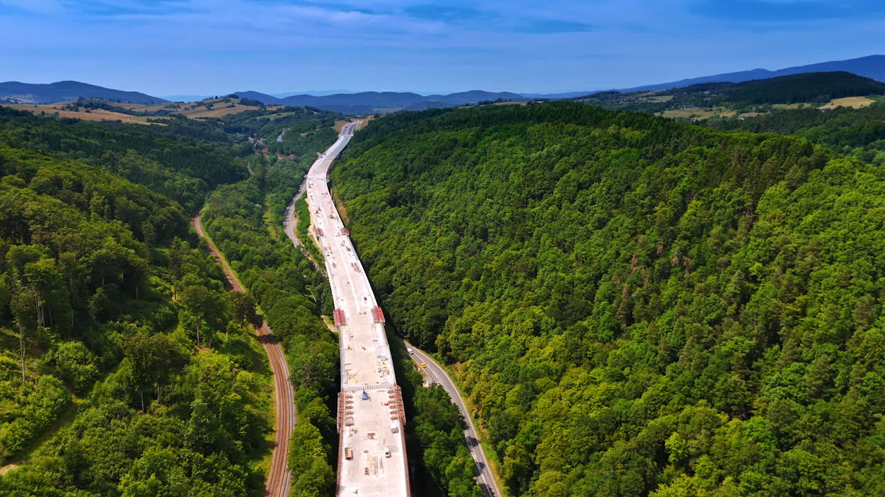 New highway project update. Heavy machinery works on a highway stretching through a green valley under a clear blue sky, showcasing progress