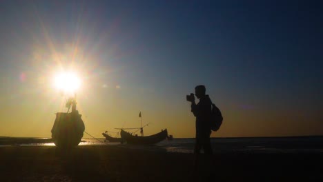 photographer capturing photo near the coastline of saint martin island. traditional sampan boats, sun and orange blue sky in the background. timelapse, silhouette