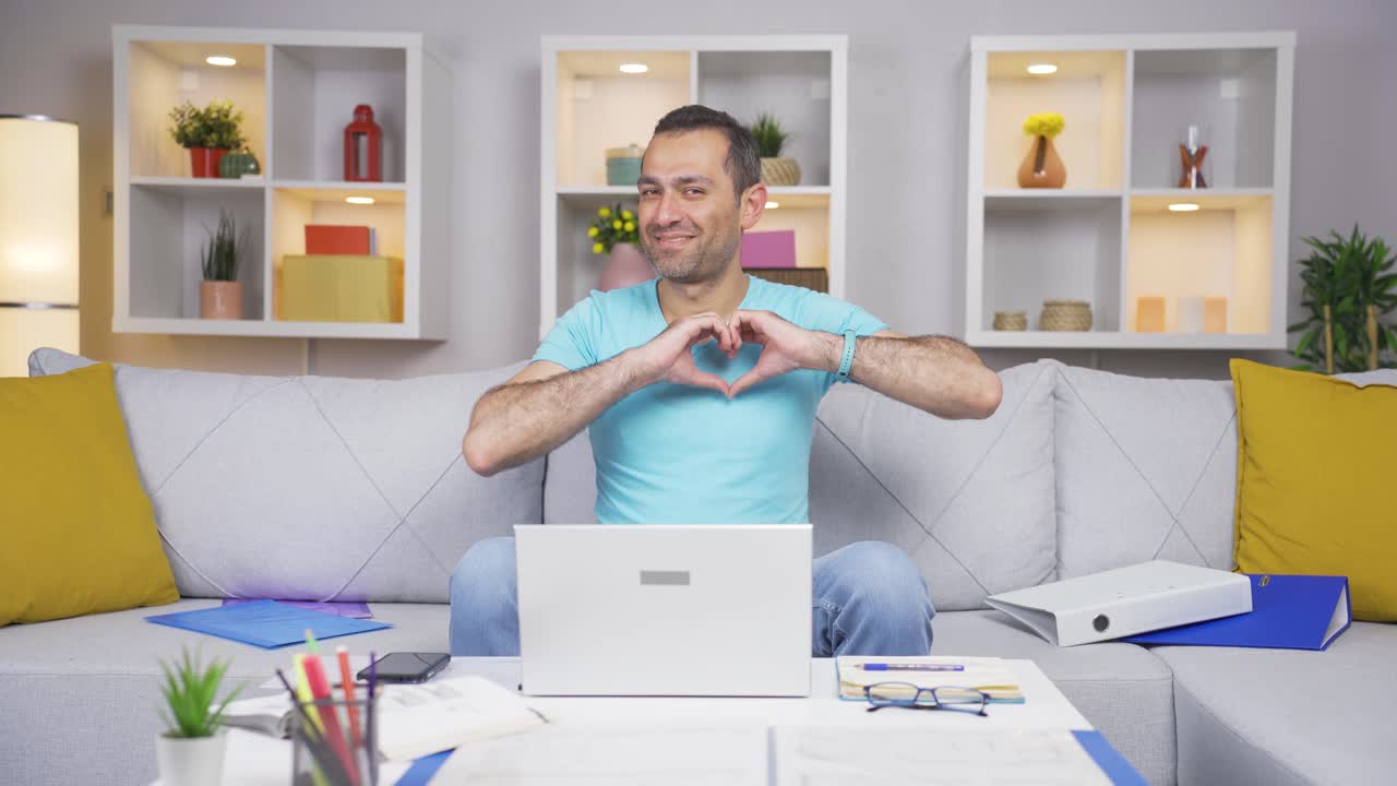 Home office worker man makes heart symbol looking at camera.