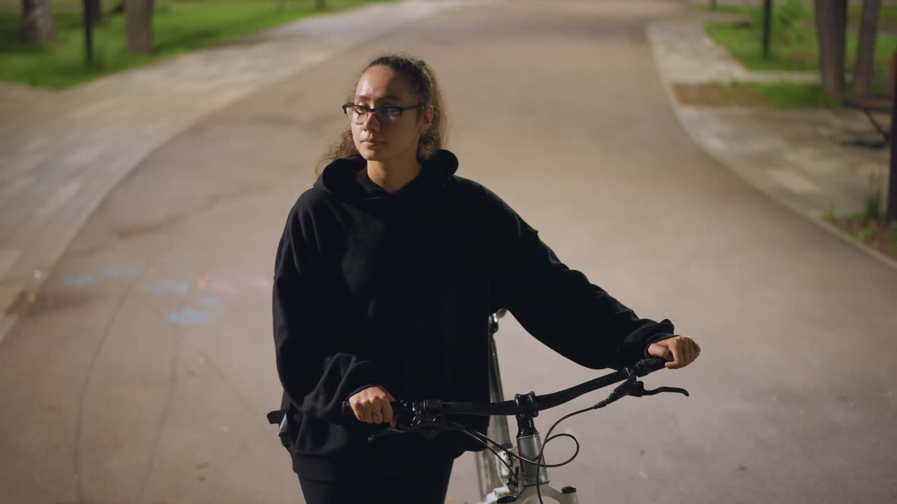 Quiet Park Scene With Woman And Bicycle At Dusk, Serene Nighttime Setting With Woman Resting On Her Bicycle Alone, Calm Evening In Empty Park Where Woman Contemplates While Leaning On Her Bicycle