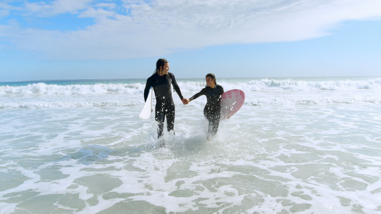 una pareja de surfistas con tablas de surf corriendo en el mar 4k