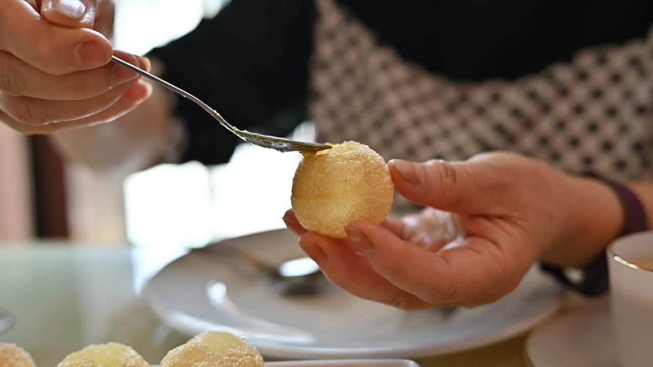 un primer plano de una mujer llenando salsa de chile en el hueco de panipuri, una popular comida callejera india.