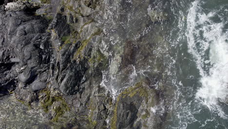 Aerial-top-down-video-of-waves-crashing-over-rocks-in-Jamestown,-Rhode-Island