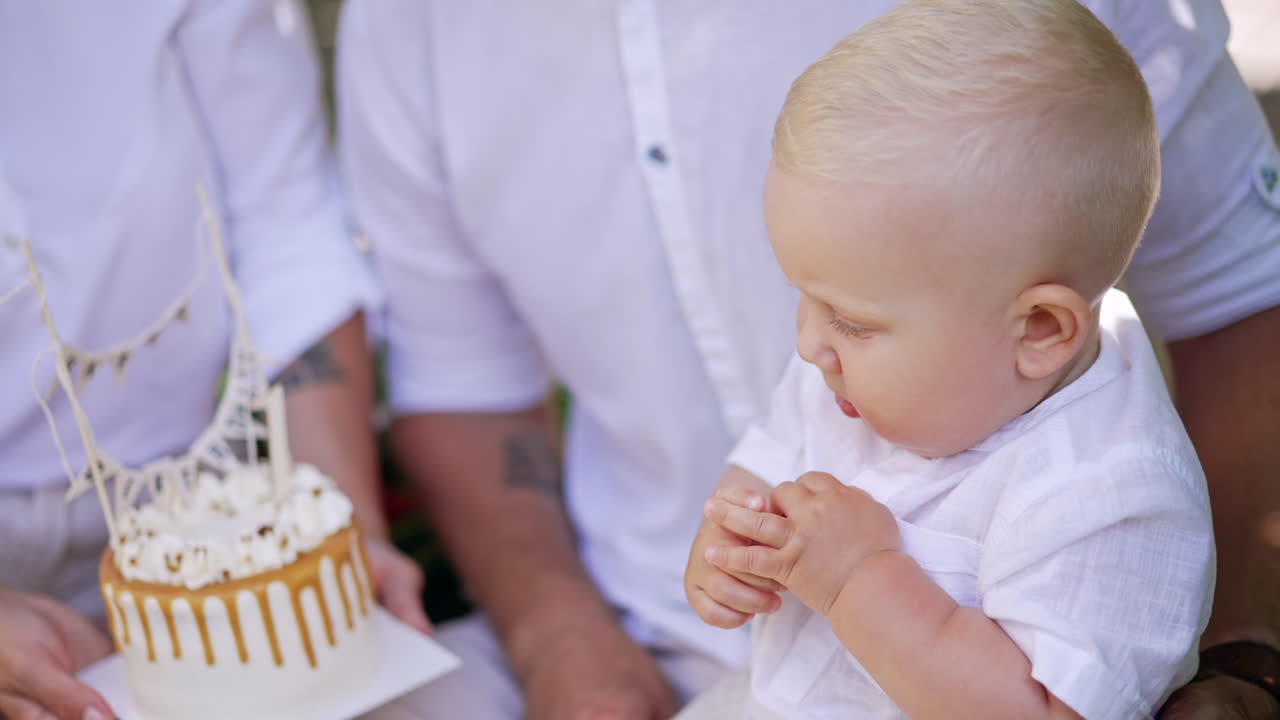 Unrecognized parents hold a cake in front of their baby. Mother shows a cake to her child. Family celebrating first kid's birthday. Close up.