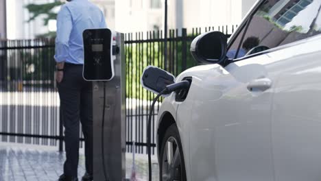 Suit-clad-businessman-with-progressive-ambition-leaning-on-his-electric-vehicle.