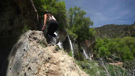 young female photographer climbing on rock under rifle falls, colorado usa, slow motion