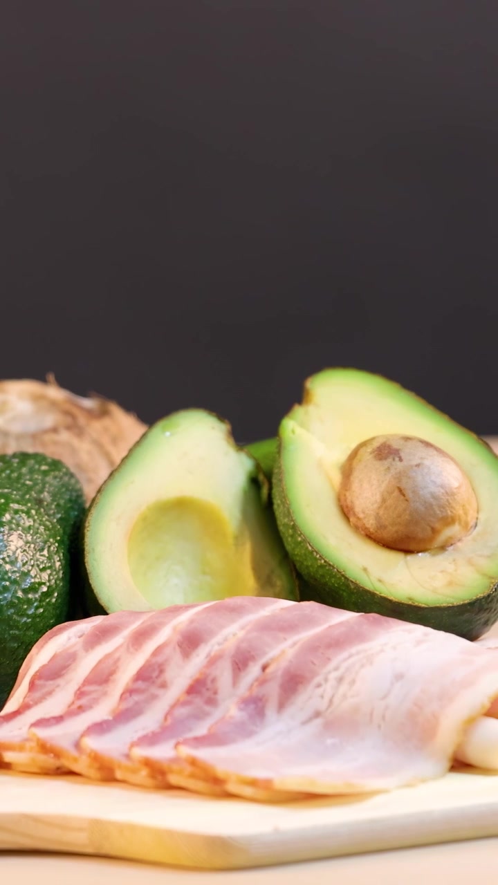 Et utvalg av sunt fett, inkludert oljer, nøtter og avokado, arrangert på et bord med myk belysning.