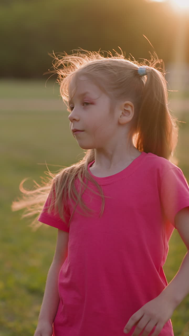 Cute girl with injured eye shakes ponytails on lush field at sunset time slow motion. Active playing in summer park. Pretty hairstyle and game